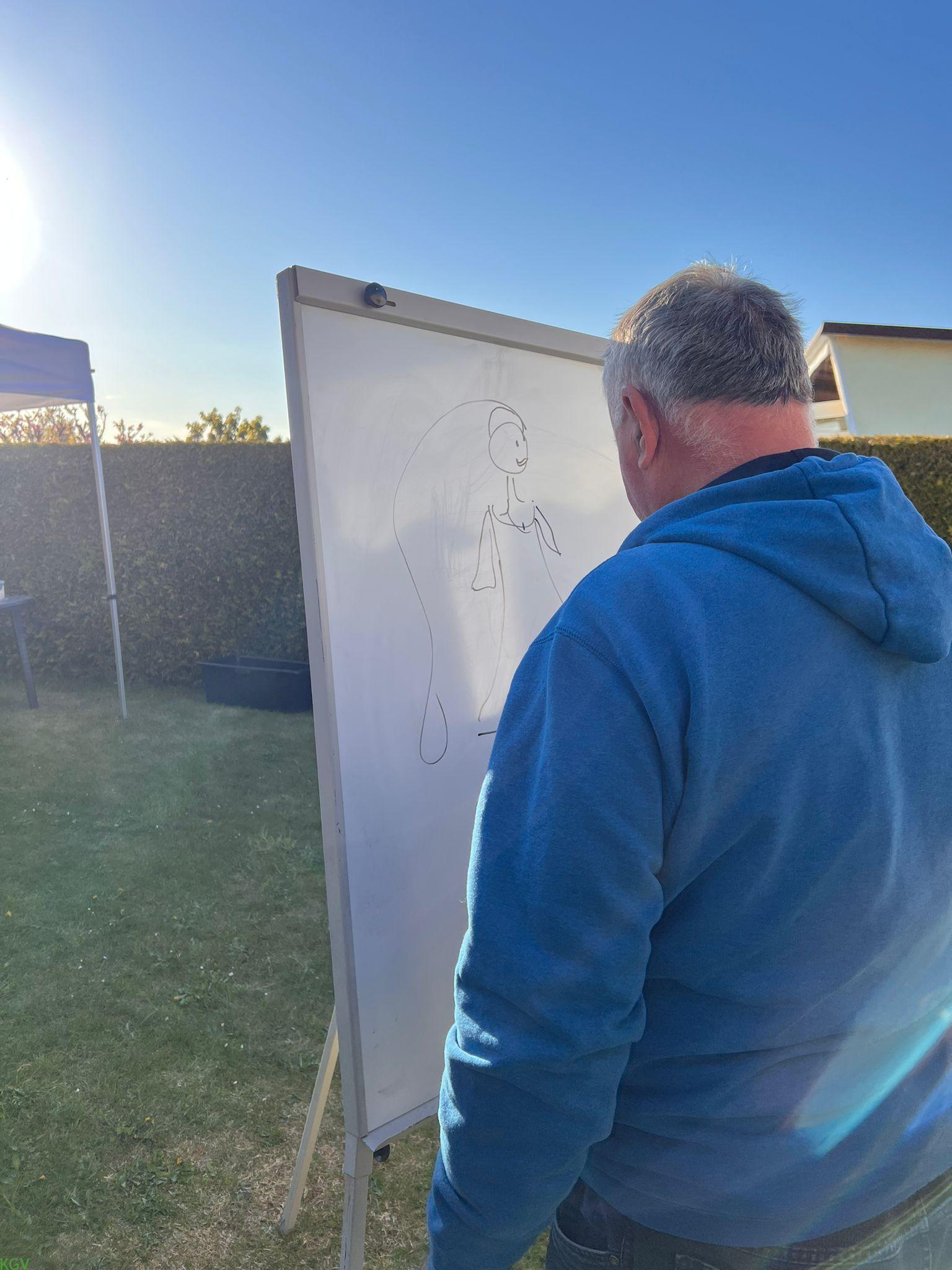 Gartenfreund im blauen Hoodie zeichnet eine Dame an das Whiteboard