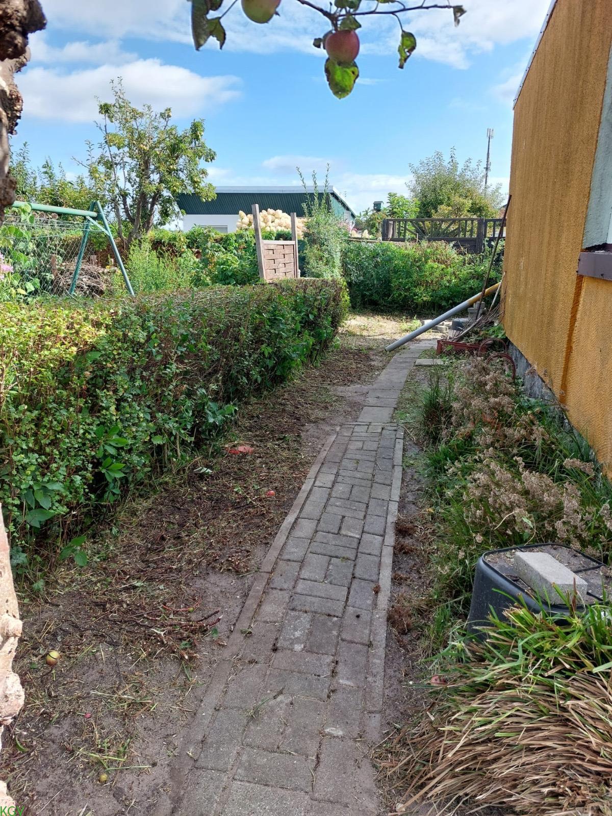 Gepflasterter Gartenweg entlang der Hecke neben der Laube