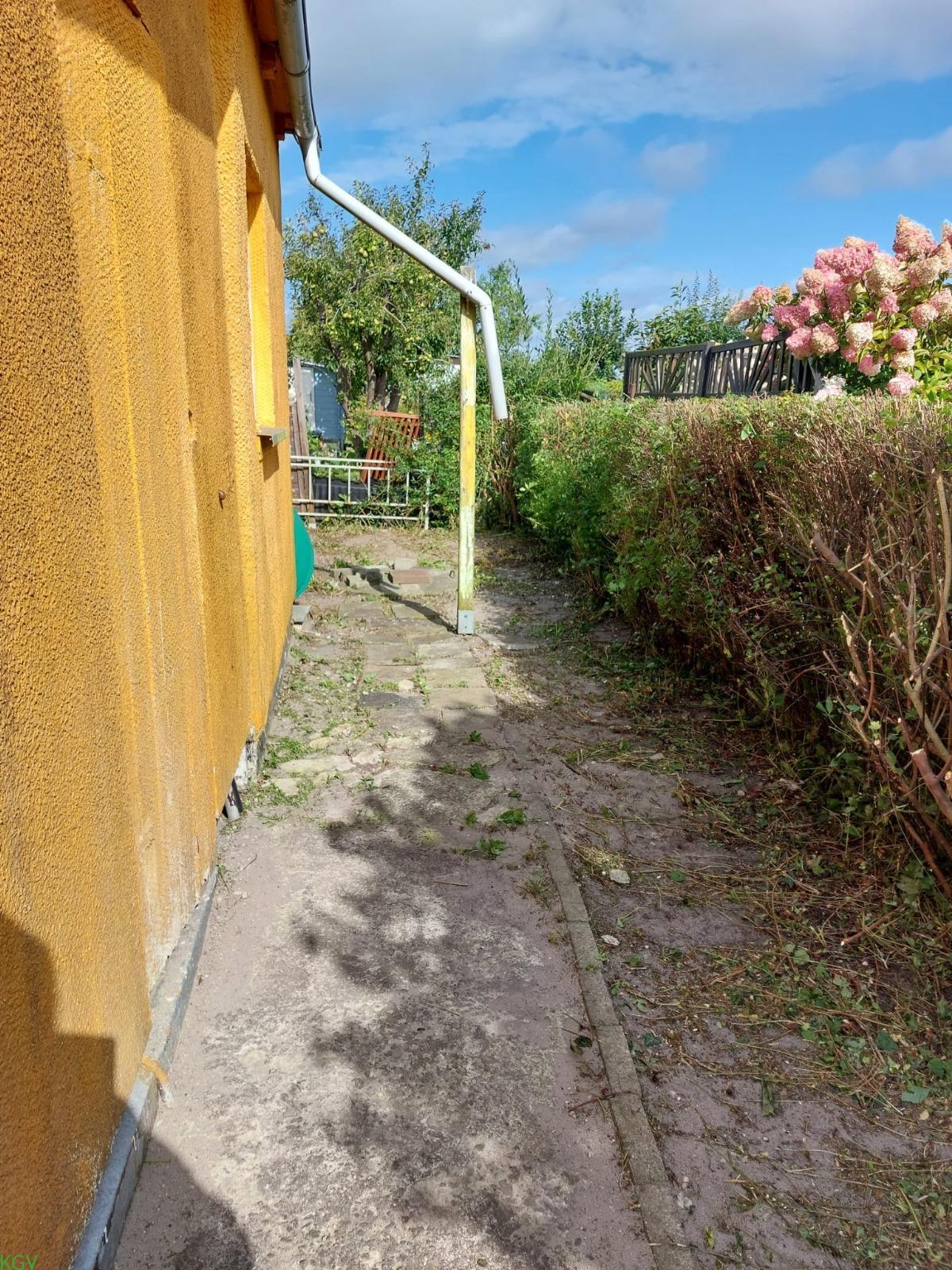 Schmaler Weg entlang der gelben Laubenwand